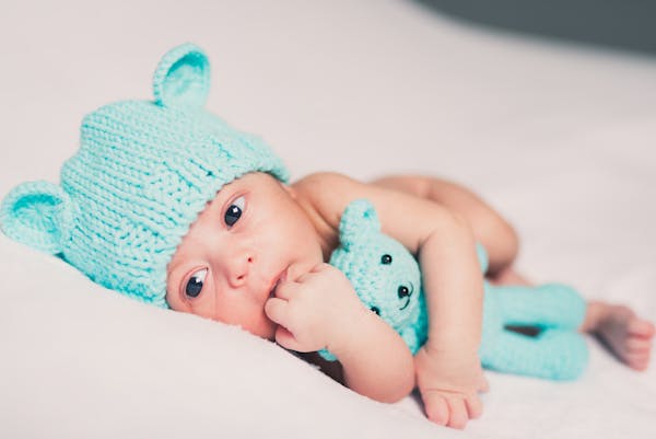 Close-up of a newborn baby wearing a cute knitted beanie and holding a matching toy.