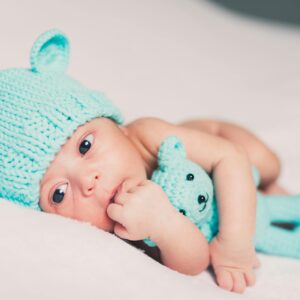 Close-up of a newborn baby wearing a cute knitted beanie and holding a matching toy.