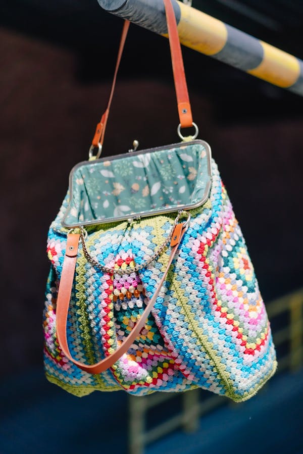 Vibrant multicolored crochet handbag with leather straps hanging on a bar.